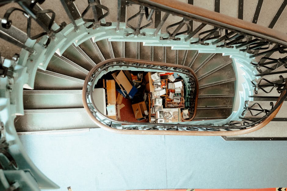 Interior view of a grand, historic building featuring high vaulted ceilings with intricate ironwork arches, large stained glass windows allowing natural light to fill the space, and ornate stone walls with detailed architectural features. A wide staircase with a decorative balustrade leads down to a lower level with patterned tiled floors. Several visitors are seen walking or standing on the staircase and around the open central area, with some approaching sculptures and historical statues displayed on pedestals. The overall atmosphere suggests a historic or cultural site, such as a museum or a cathedral, with classical architectural elements and a spacious, well-lit environment that emphasizes the building's grandeur and detailed craftsmanship, supporting the context of suitable spaces for private or independent visits that might require clear access routes for rubbish removal or maintenance activities. Waste Clearance Kensington could provide services for cleaning or clearance in similar historic interiors that demand careful handling of debris or waste within such ornate settings.